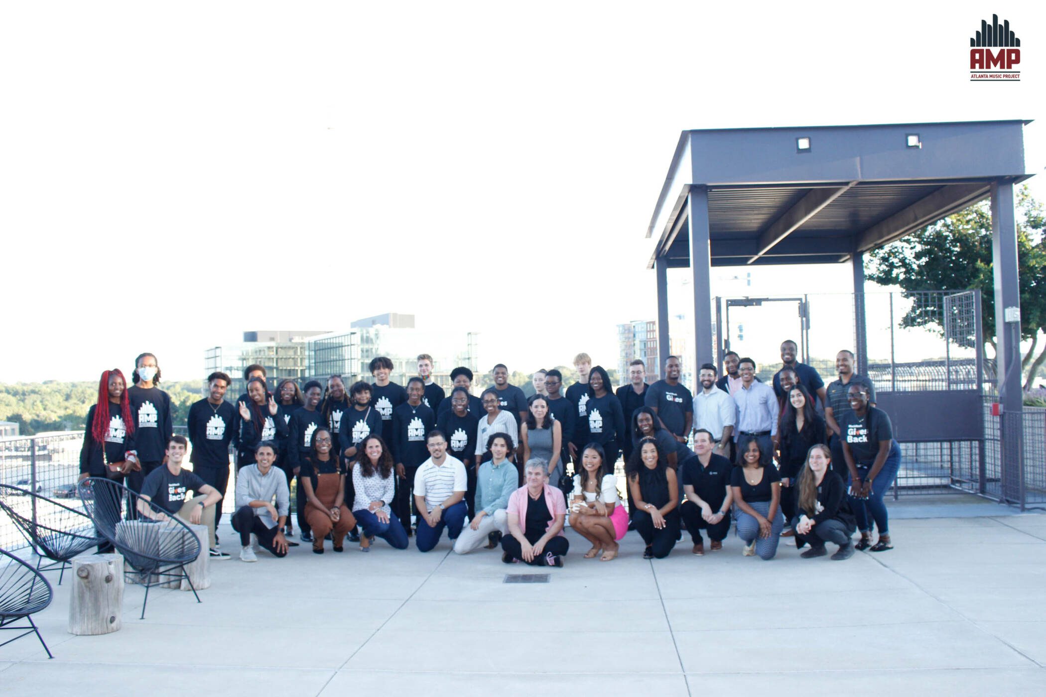 AMP students dressed in their black t-shirts with the AMP logo on front, pose with BlackRock employees on their rooftop overlooking Ponce De Leon Avenue at their Atlanta office