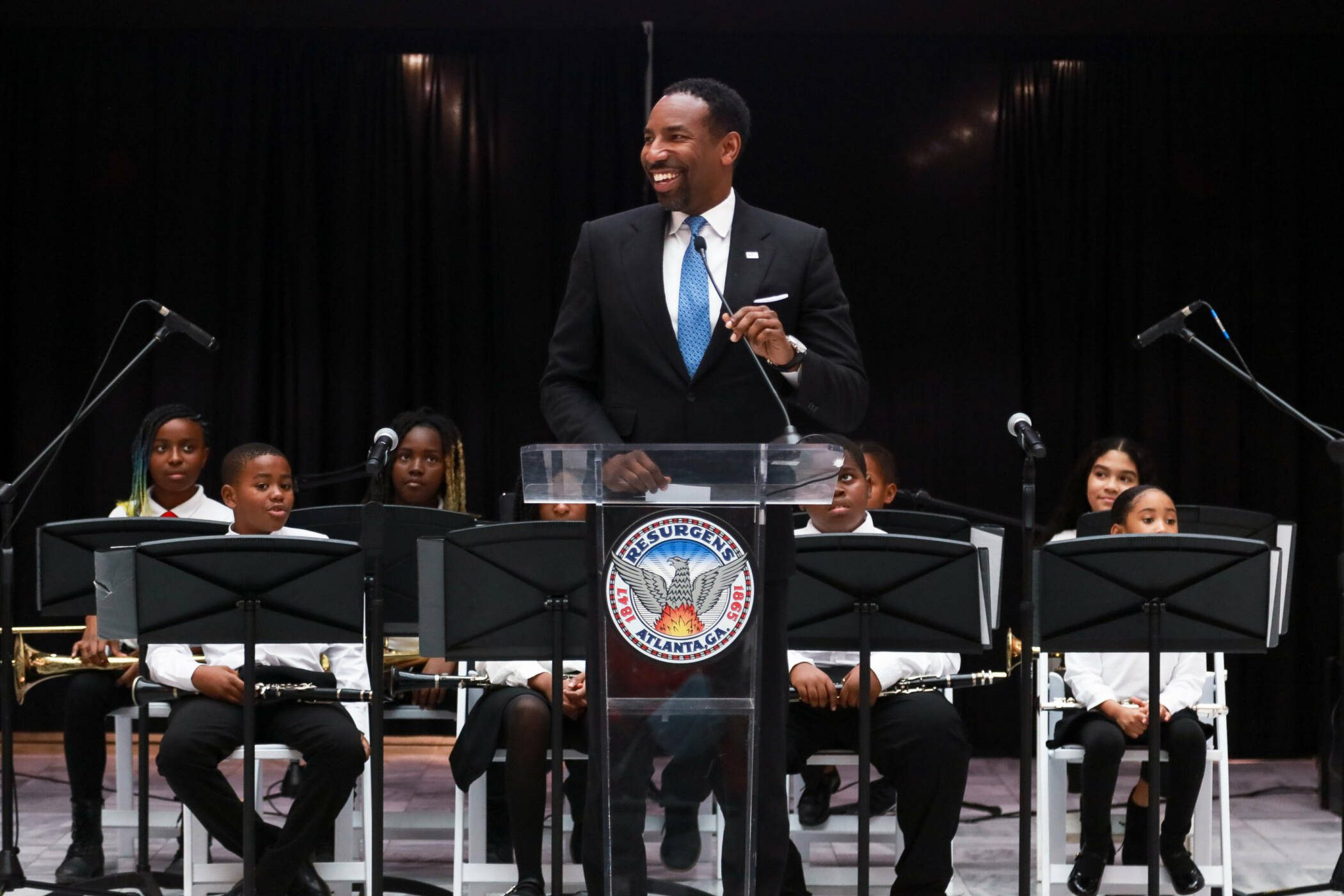Mayor of Atlanta Andre Dickens addresses attendees at Atlanta's City Hall while at a podium in front of AMP Afterschool Musicians 
